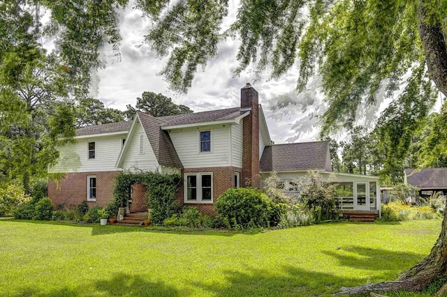 view of front of home featuring a sunroom, a chimney, a front lawn, and brick siding