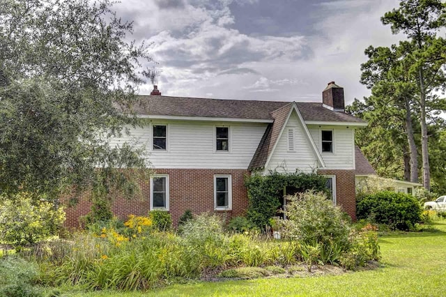 rear view of property with brick siding, a lawn, and a chimney