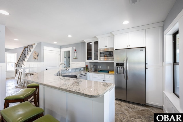 kitchen with appliances with stainless steel finishes, a peninsula, white cabinetry, a kitchen bar, and glass insert cabinets