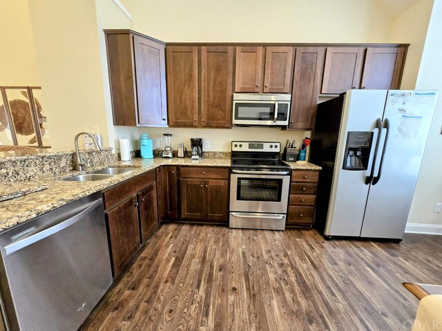 kitchen featuring appliances with stainless steel finishes, dark wood-style flooring, a sink, and light stone countertops