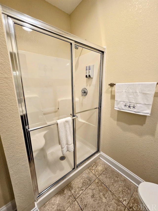 full bath featuring toilet, a stall shower, baseboards, and tile patterned floors