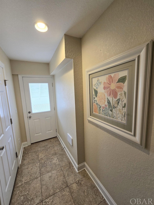 doorway with baseboards and a textured wall