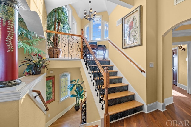 stairs with arched walkways, wood finished floors, a towering ceiling, and baseboards