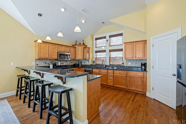 kitchen featuring brown cabinets, decorative light fixtures, stainless steel appliances, a sink, and dark stone counters