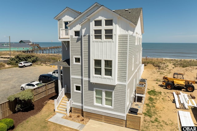 exterior space with board and batten siding, a water view, fence, and roof with shingles