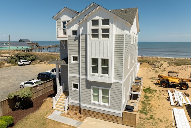 exterior space featuring entry steps, a water view, fence, roof with shingles, and board and batten siding