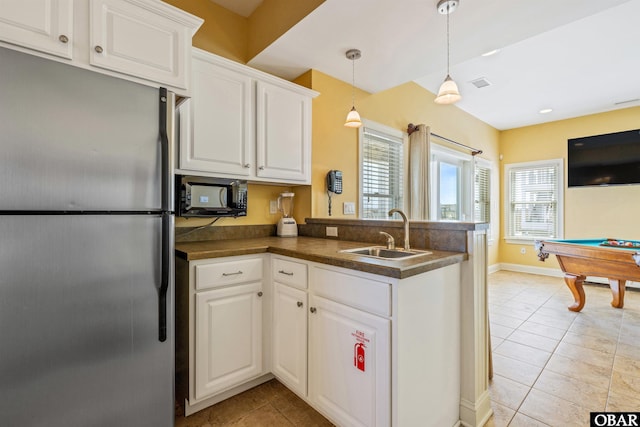 kitchen with dark countertops, a sink, freestanding refrigerator, and white cabinets