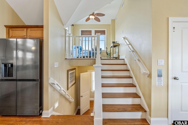 stairway with lofted ceiling, wood finished floors, visible vents, baseboards, and a ceiling fan