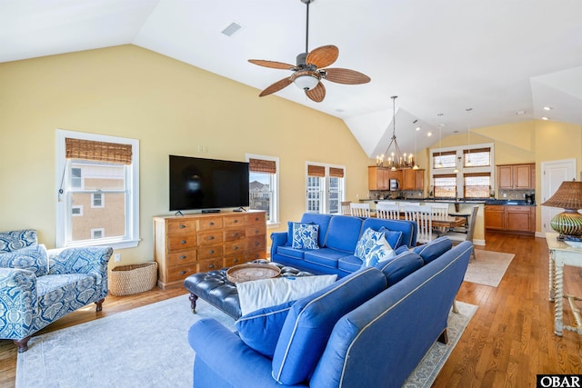 living room with high vaulted ceiling, ceiling fan with notable chandelier, visible vents, and wood finished floors