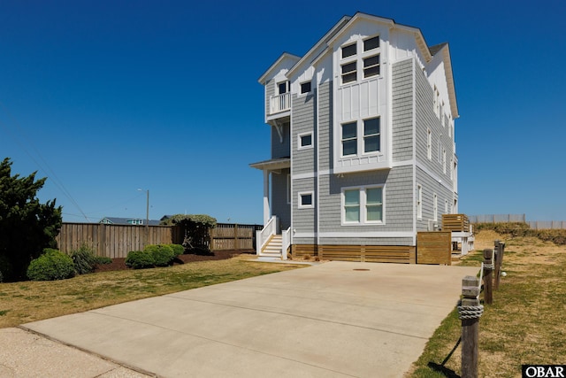 view of front facade with entry steps, a front lawn, fence, and a balcony