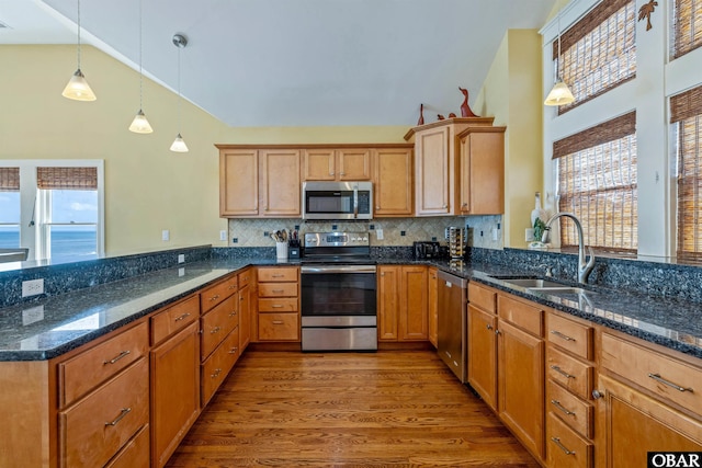 kitchen with dark stone counters, stainless steel appliances, hanging light fixtures, and a sink