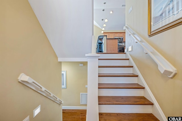 stairway with baseboards, visible vents, a high ceiling, and wood finished floors