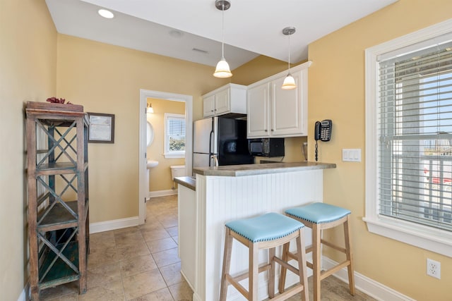 kitchen featuring black microwave, a peninsula, white cabinets, freestanding refrigerator, and decorative light fixtures