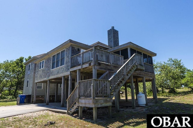 rear view of property with a sunroom, a chimney, concrete driveway, and stairs