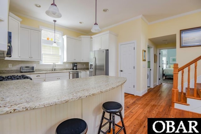 102 William And Mary Way Lot 13, Manteo, NC 27954 - kitchen featuring appliances with stainless steel finishes, a peninsula, ornamental molding, light wood-style floors, and decorative light fixtures