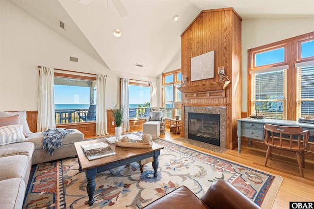 living area with a fireplace with flush hearth, visible vents, high vaulted ceiling, and wood finished floors