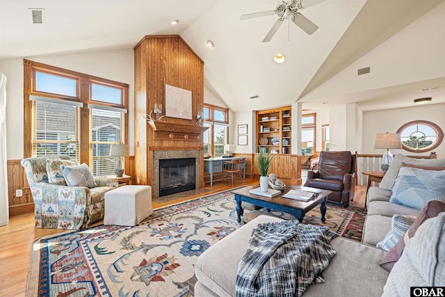 living area featuring visible vents, built in features, a wainscoted wall, a premium fireplace, and wood finished floors