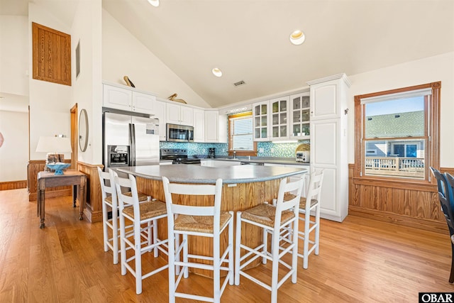 kitchen featuring stainless steel appliances, a breakfast bar, white cabinets, and wainscoting