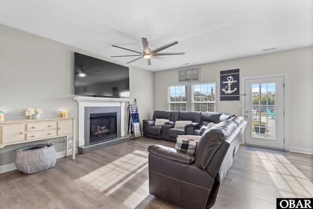 living room featuring wood finished floors, ceiling fan, a tile fireplace, baseboards, and visible vents