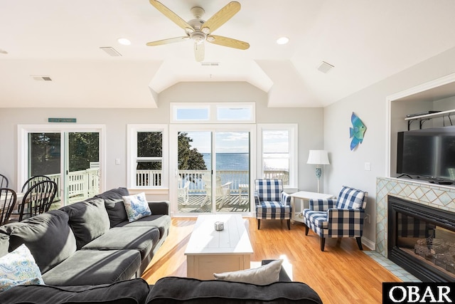 living area with visible vents, a tiled fireplace, lofted ceiling, ceiling fan, and wood finished floors