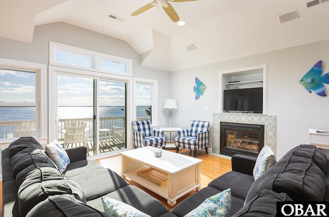 living area with lofted ceiling, light wood-style flooring, a water view, visible vents, and a tiled fireplace