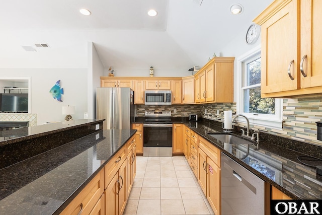 kitchen featuring appliances with stainless steel finishes, a sink, dark stone countertops, and light tile patterned floors