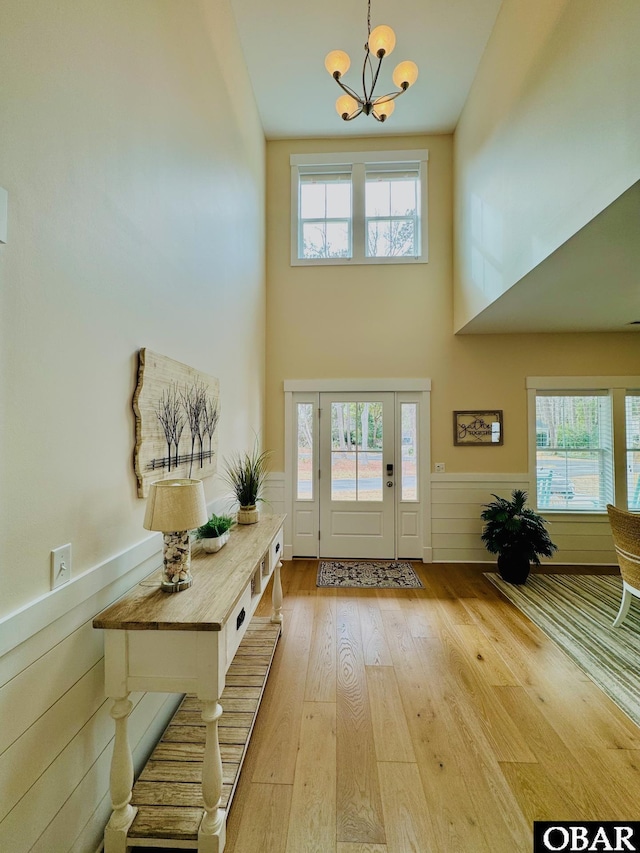 foyer entrance featuring a wainscoted wall, light wood-type flooring, a wealth of natural light, and a notable chandelier