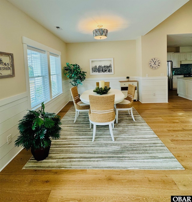 dining room with lofted ceiling, light wood-style flooring, wainscoting, and visible vents