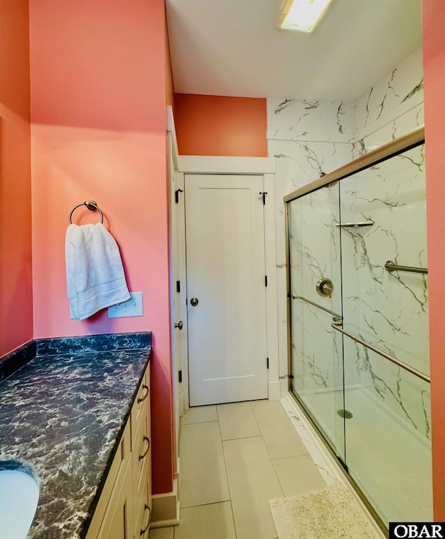 bathroom featuring tile patterned flooring, a marble finish shower, and vanity