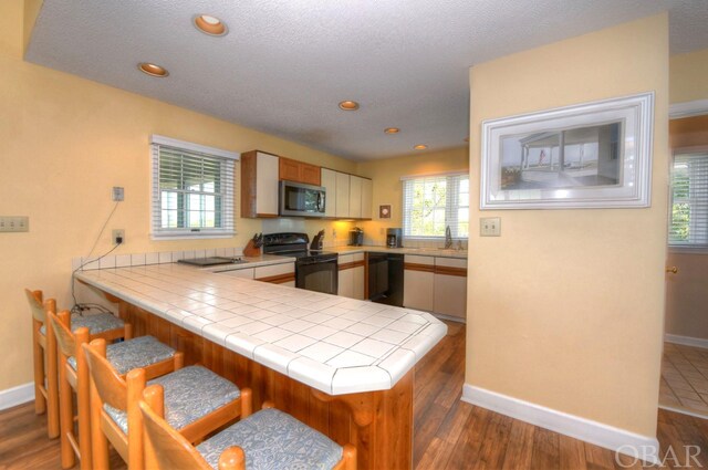 kitchen with plenty of natural light, tile countertops, a peninsula, black appliances, and a sink