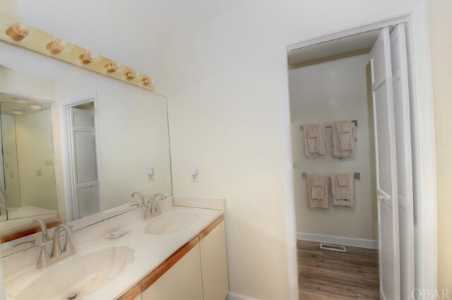 full bathroom with double vanity, a sink, baseboards, and wood finished floors