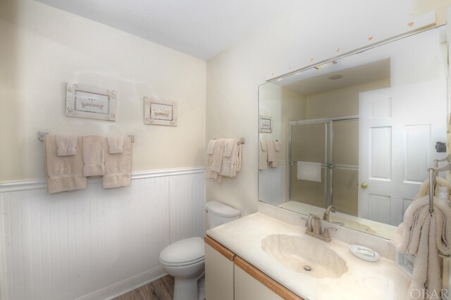 full bathroom with toilet, a wainscoted wall, wood finished floors, vanity, and a stall shower