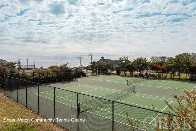 view of tennis court with a water view and fence