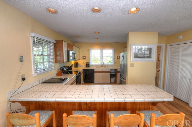 kitchen with a peninsula, a sink, tile counters, black appliances, and a kitchen bar