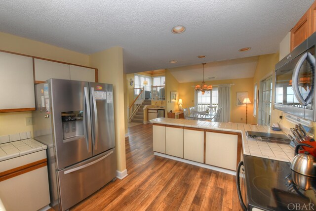 kitchen with white cabinets, tile countertops, dark wood-type flooring, decorative light fixtures, and stainless steel appliances