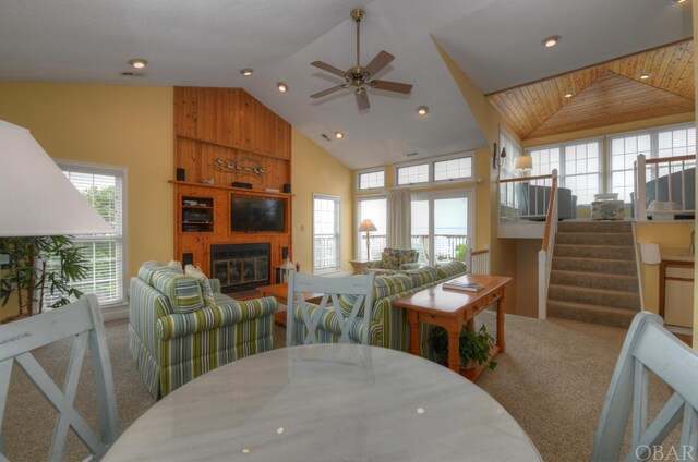 dining room featuring a ceiling fan, stairway, carpet, a fireplace, and high vaulted ceiling