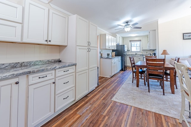 kitchen with freestanding refrigerator, dark wood-style flooring, white cabinetry, and light stone countertops