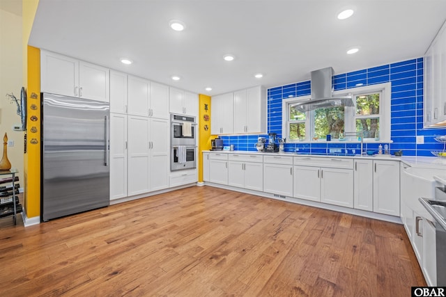 41 Eagles Nest Ln Lot 372, Southern Shores, NC 27949 - kitchen featuring appliances with stainless steel finishes, island exhaust hood, tasteful backsplash, light wood-type flooring, and white cabinets