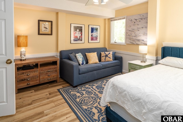 bedroom featuring ceiling fan, light wood-style flooring, and a wainscoted wall