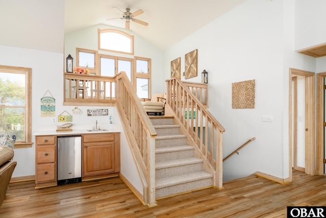 stairway with ceiling fan, baseboards, wet bar, wood finished floors, and lofted ceiling