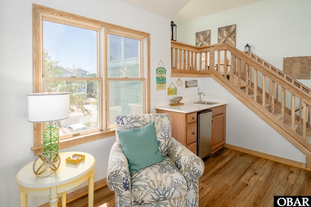 sitting room with light wood finished floors, baseboards, wet bar, vaulted ceiling, and stairway