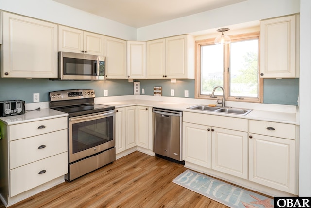 kitchen featuring cream cabinets, appliances with stainless steel finishes, a sink, light countertops, and light wood-type flooring