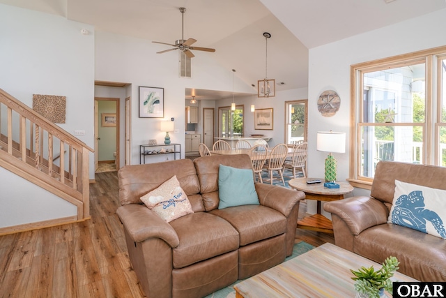 living area with high vaulted ceiling, ceiling fan, stairs, and wood finished floors