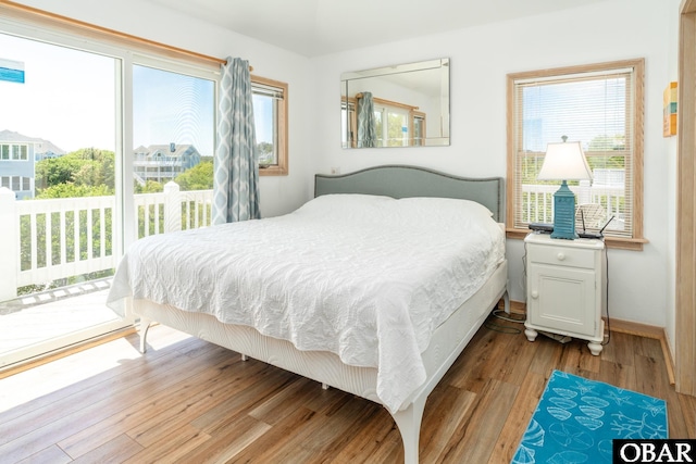 bedroom with access to outside, baseboards, multiple windows, and wood finished floors