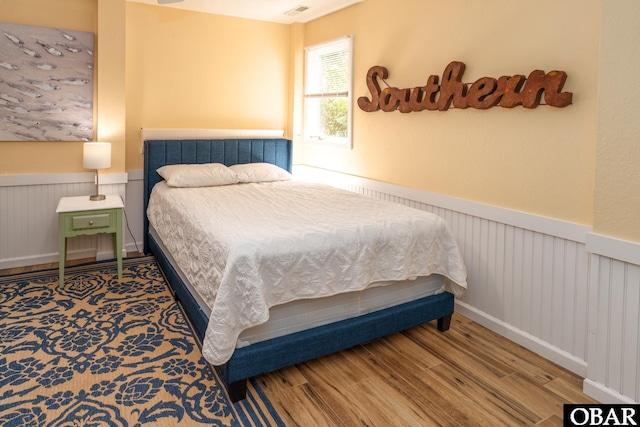 bedroom with a wainscoted wall, wood finished floors, and visible vents