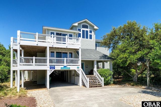 coastal home featuring a shingled roof, a porch, stairway, concrete driveway, and a carport