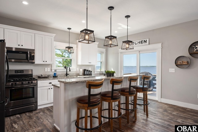 kitchen with light stone counters, a center island, stainless steel appliances, white cabinets, and baseboards