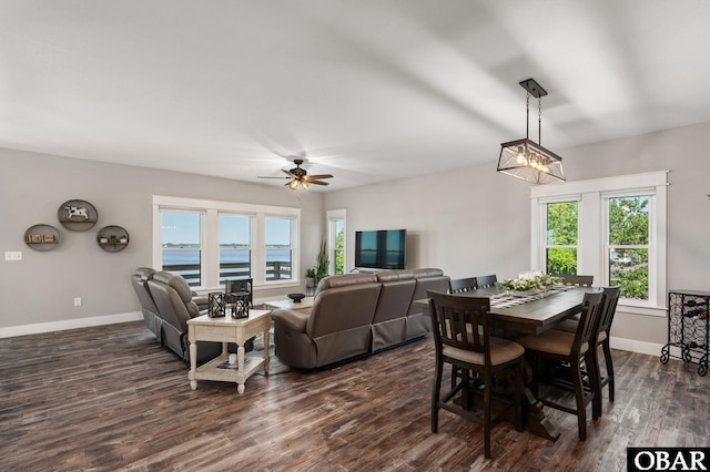 dining area featuring ceiling fan with notable chandelier, dark wood finished floors, and baseboards