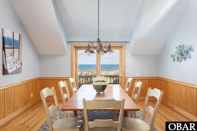 dining space with a water view, an inviting chandelier, light wood-type flooring, and wainscoting