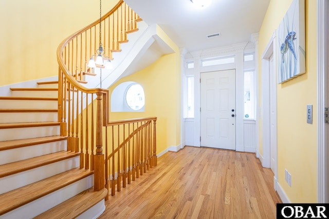 foyer entrance with baseboards, stairway, visible vents, and light wood-style floors